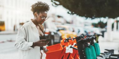 Young woman using her phone to hire an e-scooter